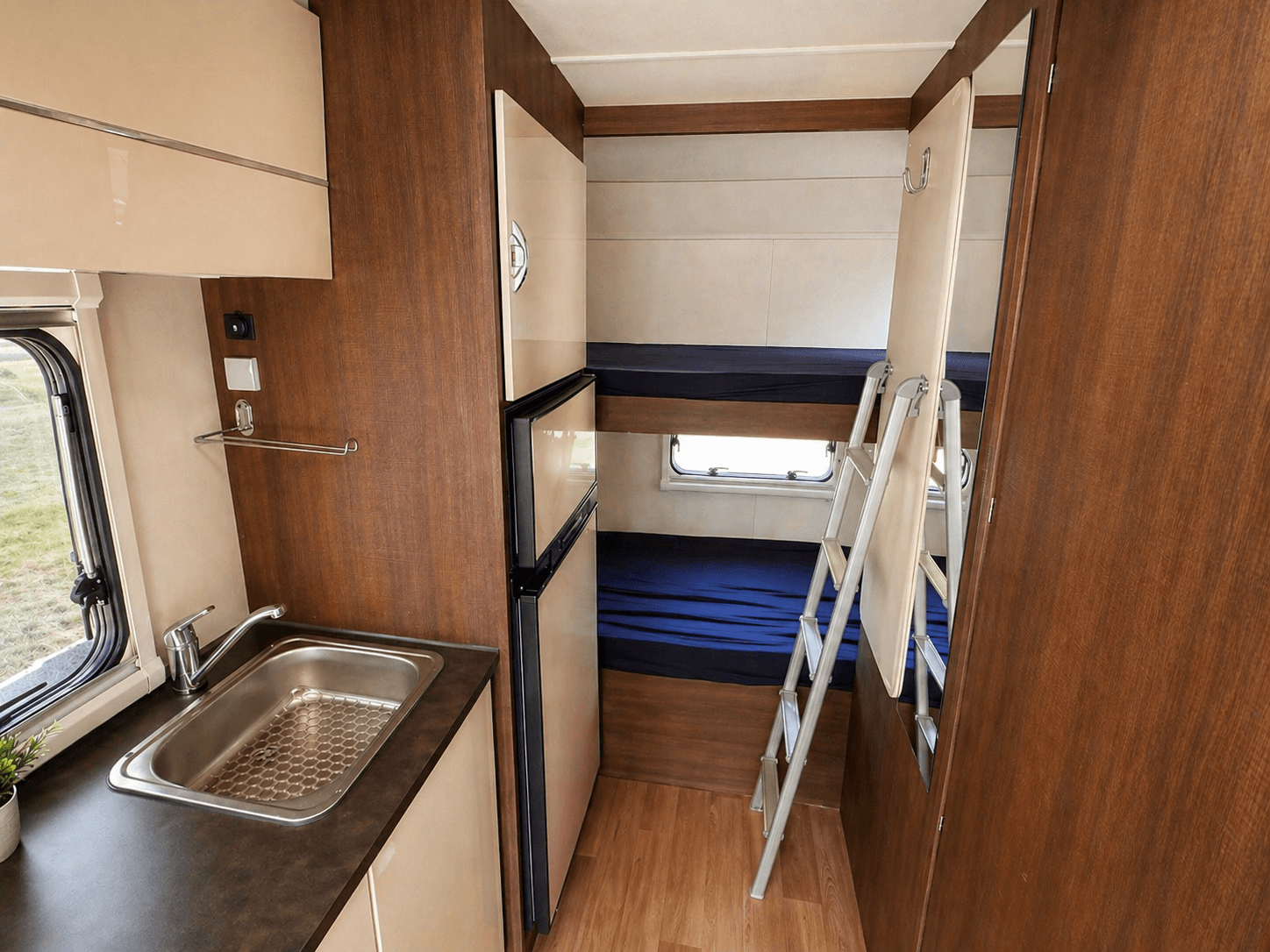 Kueche, Kuehlschrank und Etagenbetten im Wohnmobil mit ausgeklappter Leiter